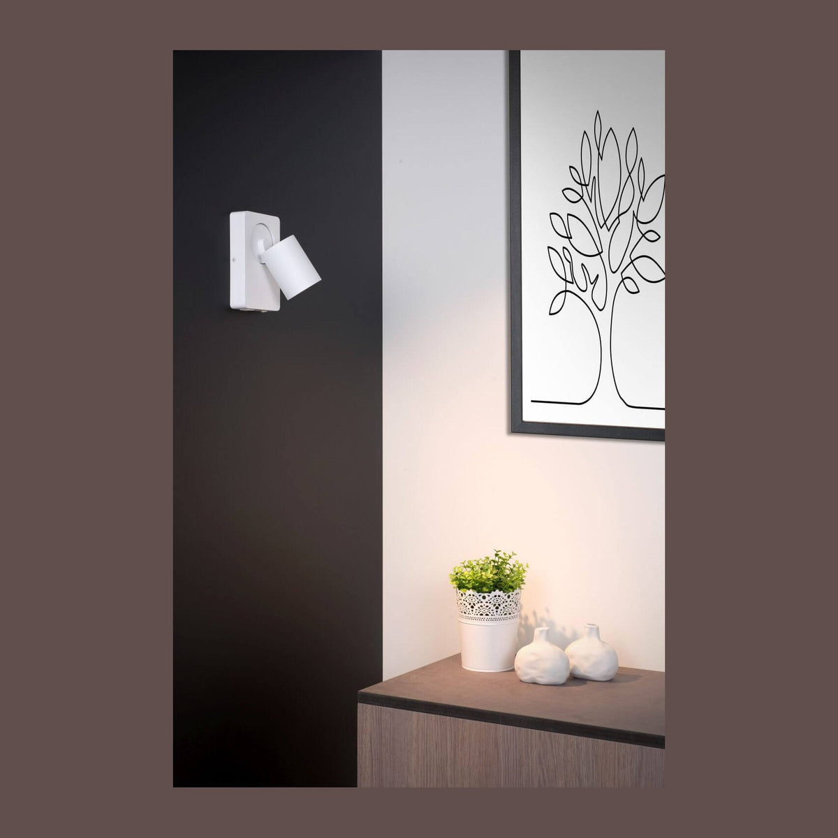 Applique murale blanche fixée sur mur noir, ambiance intérieure avec cadre et plante.