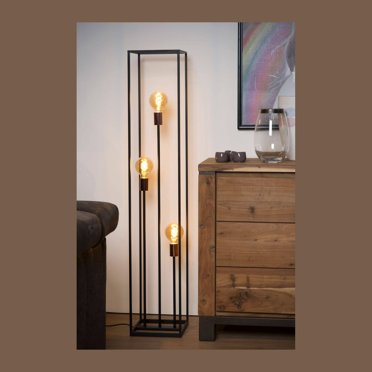 Lampadaire noir à trois ampoules dorées posé près d’un meuble en bois