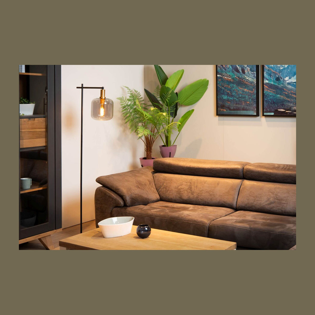 Lampadaire allumé dans un salon moderne, près d'un canapé en cuir marron et de plantes vertes.