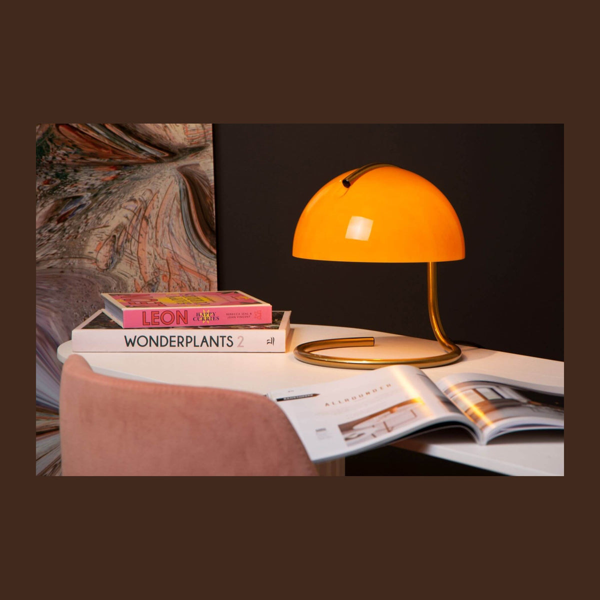 Lampe orange allumée posée sur une table blanche entourée de livres