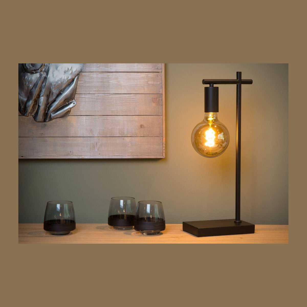 Lampe à poser noire sur console en bois, verres et mur vert olive