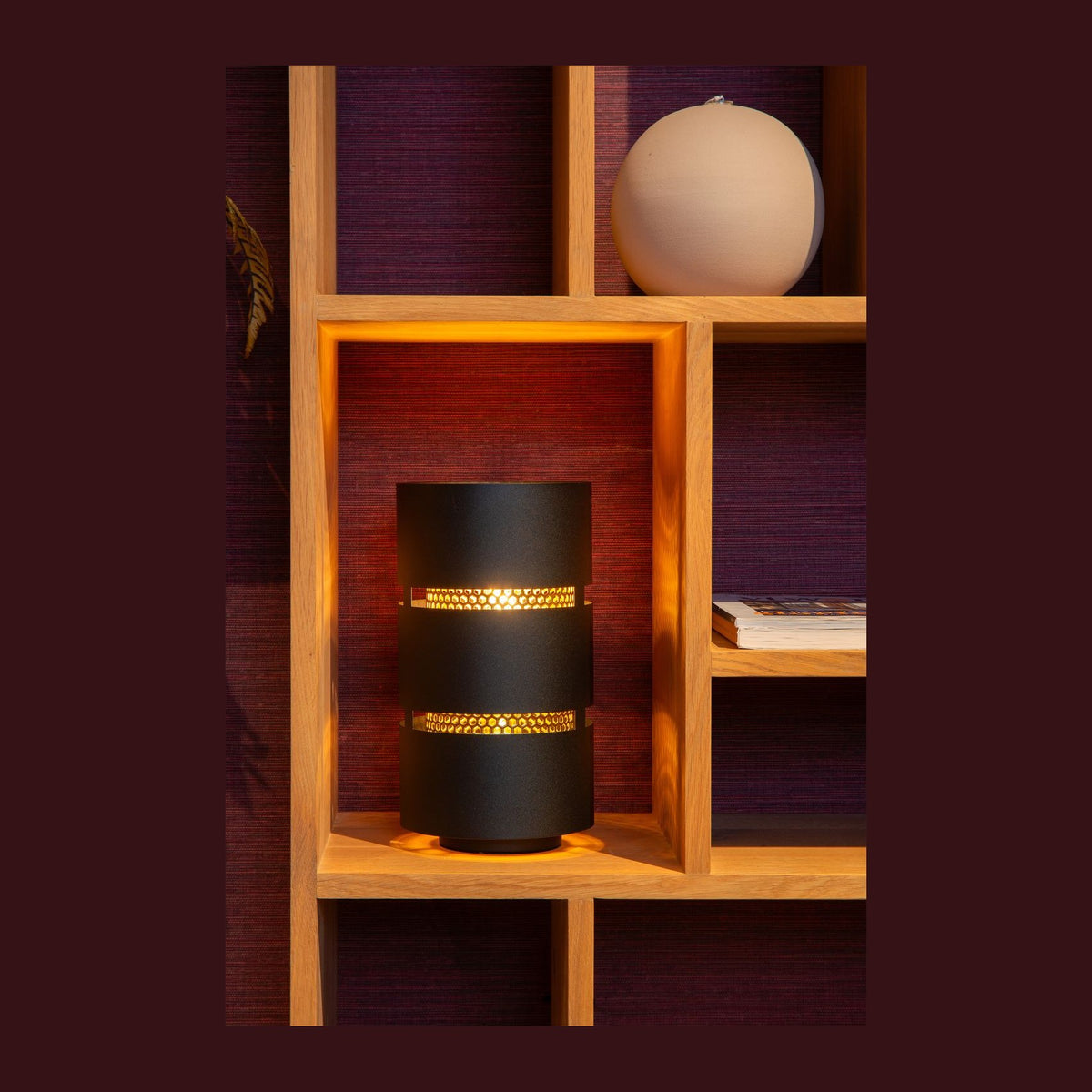 Lampe à poser cylindrique noire et dorée dans une niche en bois, ambiance chaleureuse