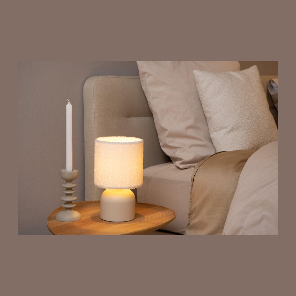 Lampe à poser beige posée sur une table de nuit en bois, ambiance chambre chaleureuse