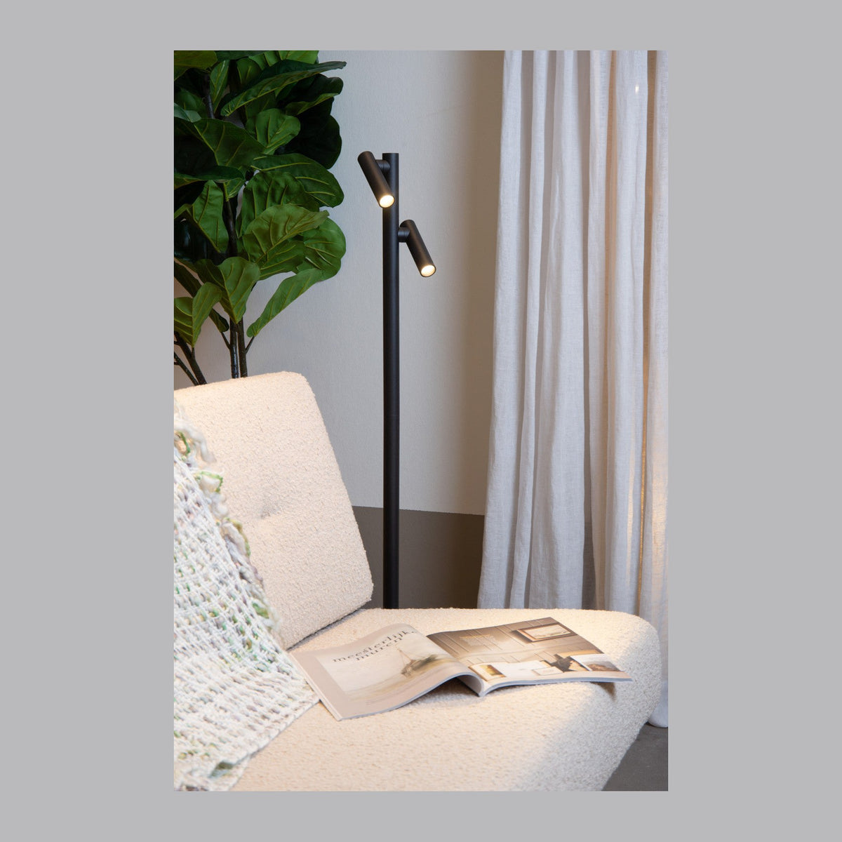 Lampadaire noir allumé dans un salon, près d'un fauteuil et d'une plante verte.