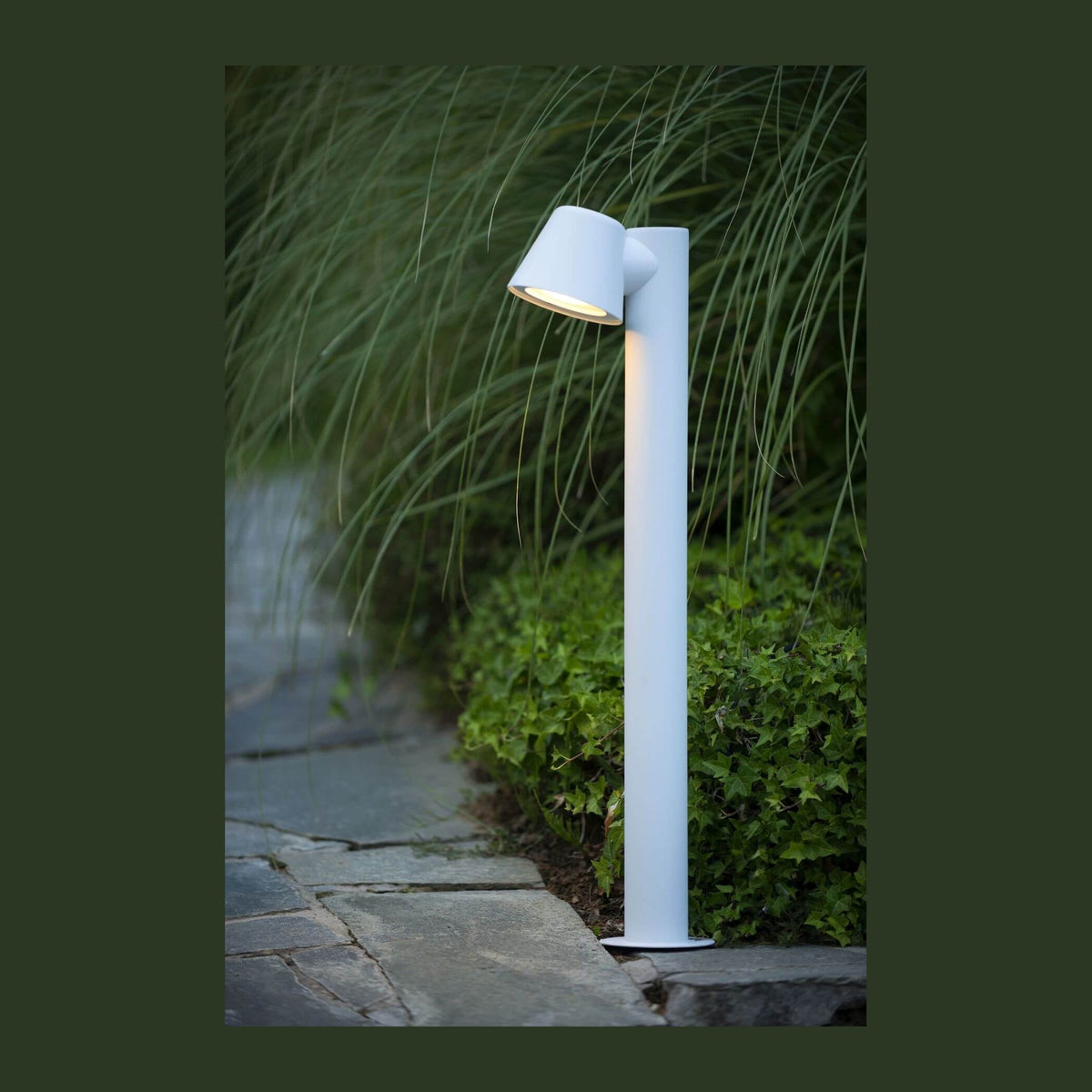 Borne lumineuse blanche installée dans un jardin près d'une allée en pierre.