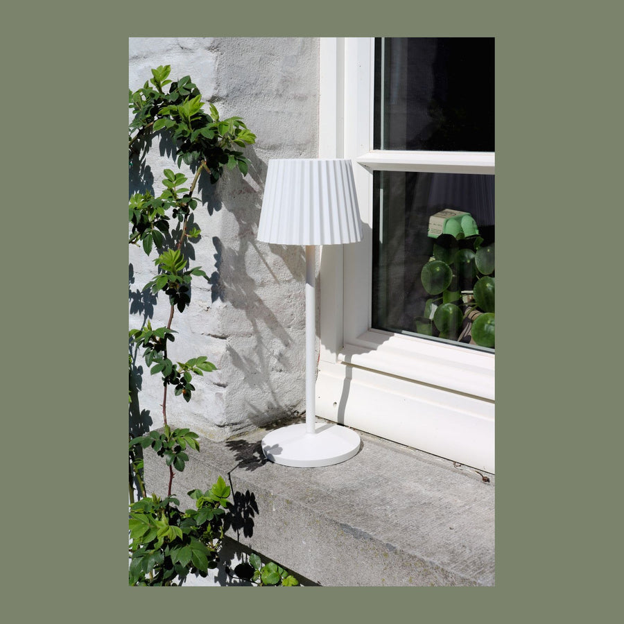 Lampe blanche posée sur un rebord en pierre devant un mur et une plante grimpante