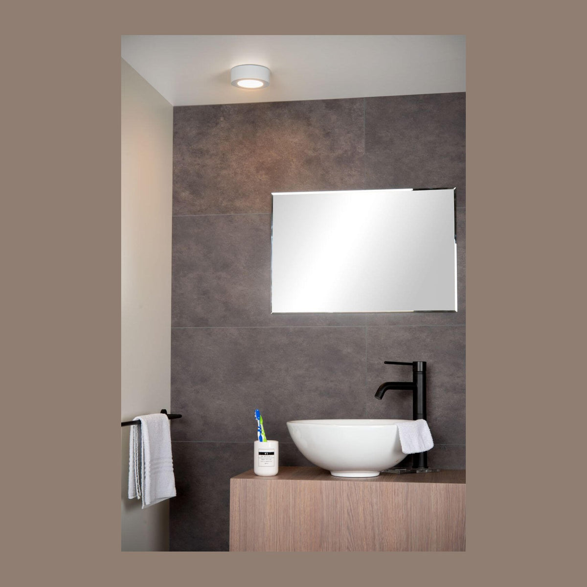 Plafonnier blanc allumé au plafond d'une salle de bain, au-dessus d'un miroir