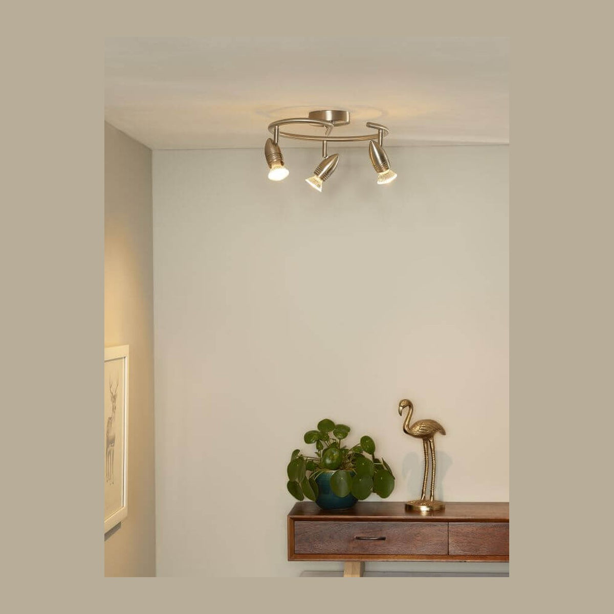 Plafonnier trois spots allumé au plafond dans un salon, meuble en bois et plante