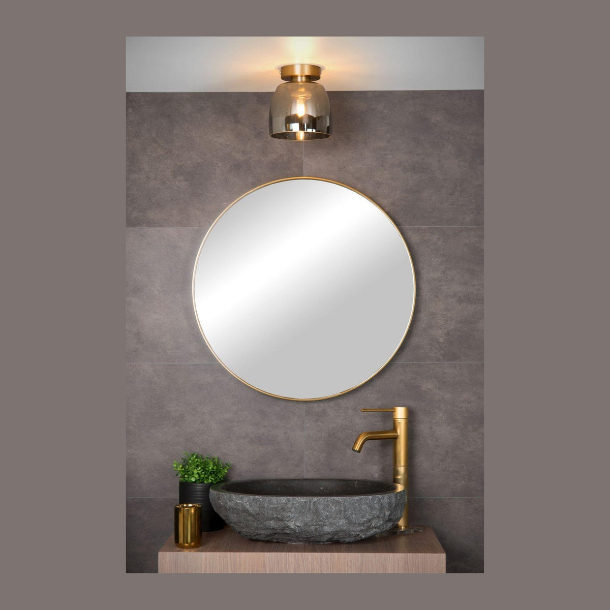 Plafonnier doré et verre fumé allumé au-dessus d'un miroir rond dans une salle de bain.