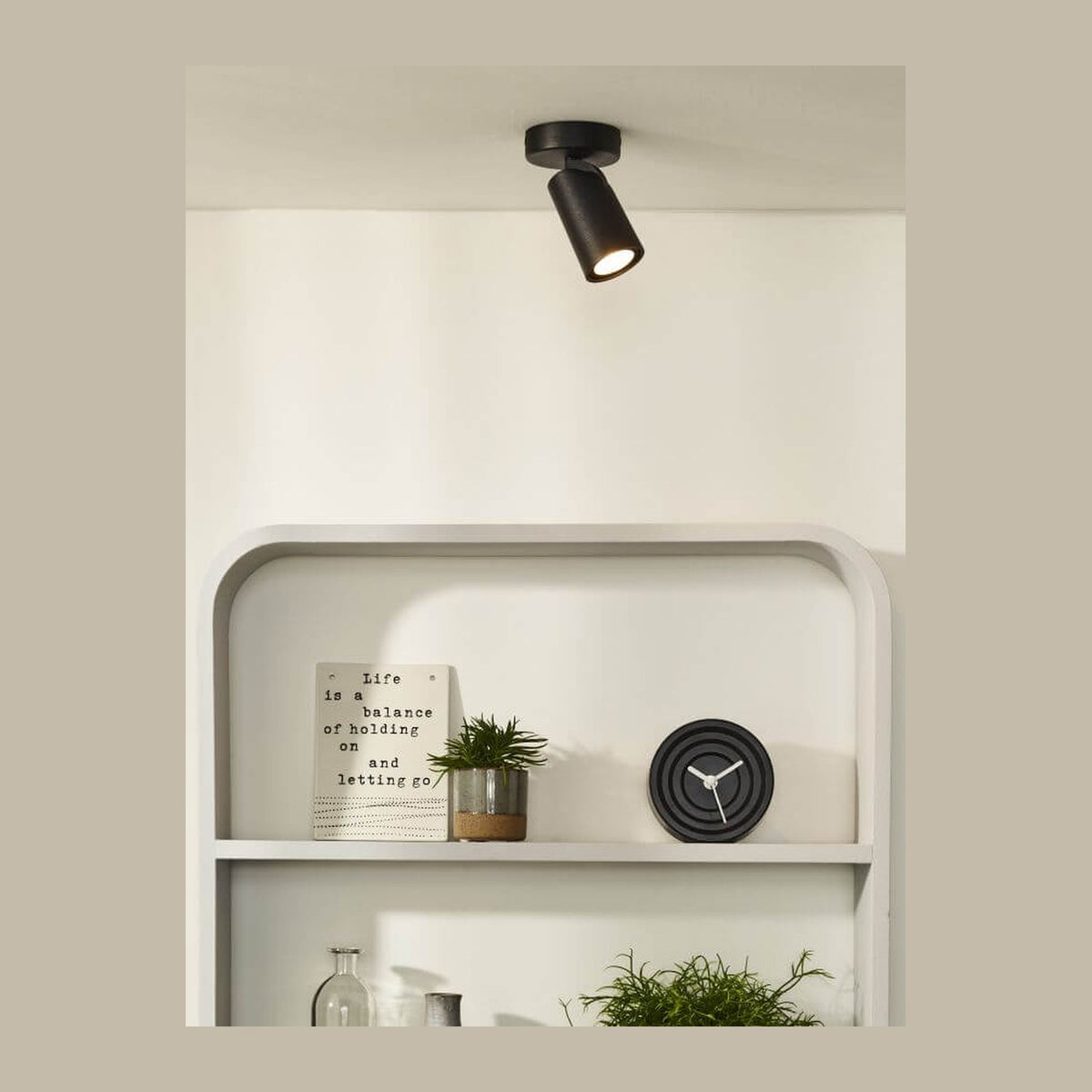 Spot plafonnier noir orientable fixé au plafond, éclairant une étagère blanche garnie de décoration