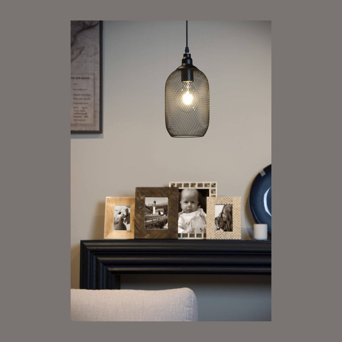 Suspension noire en maille métallique allumée au-dessus d'une cheminée décorée de cadres photo.