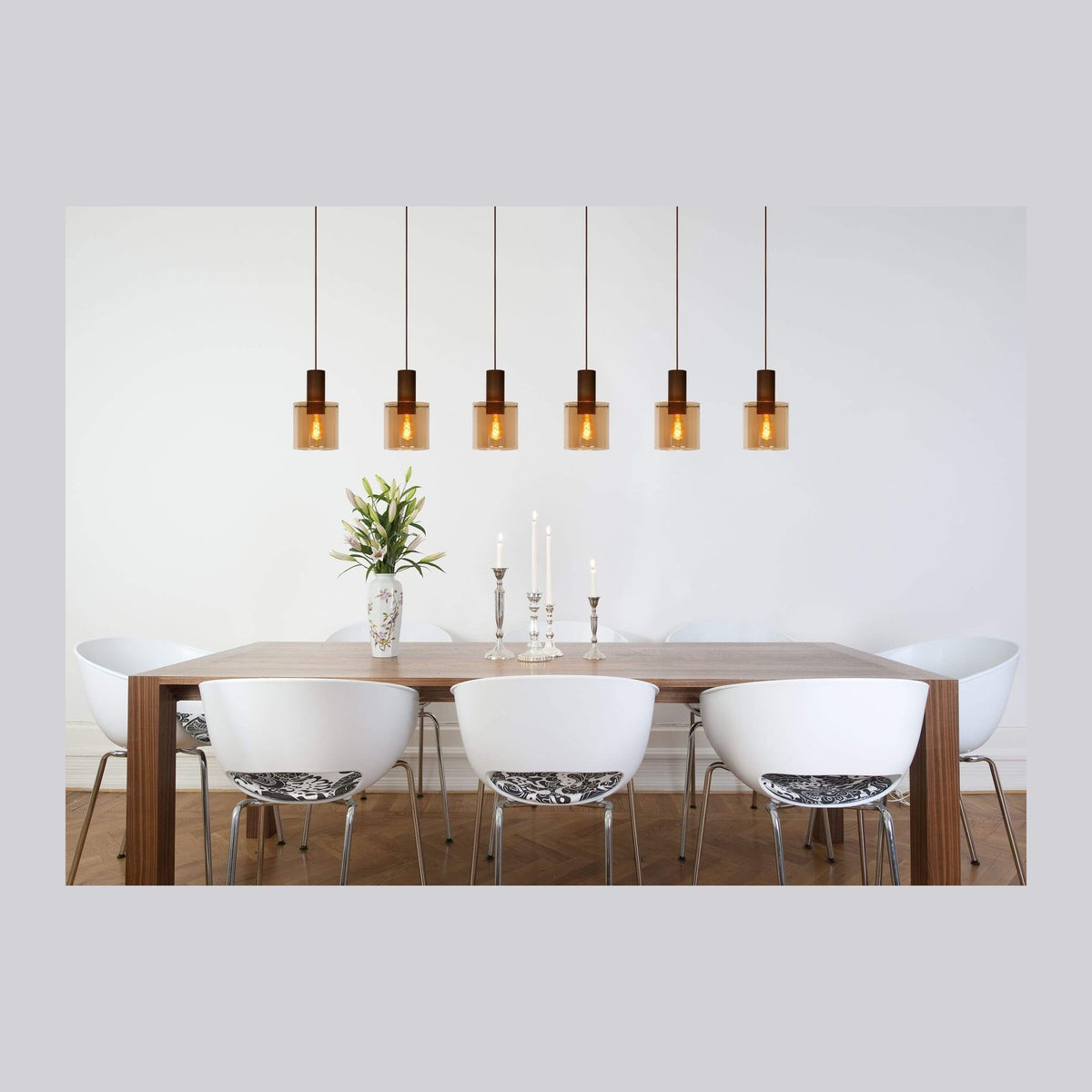 Vue d'ensemble d'une salle à manger avec suspension aux verres ambrés alignés au-dessus de la table.