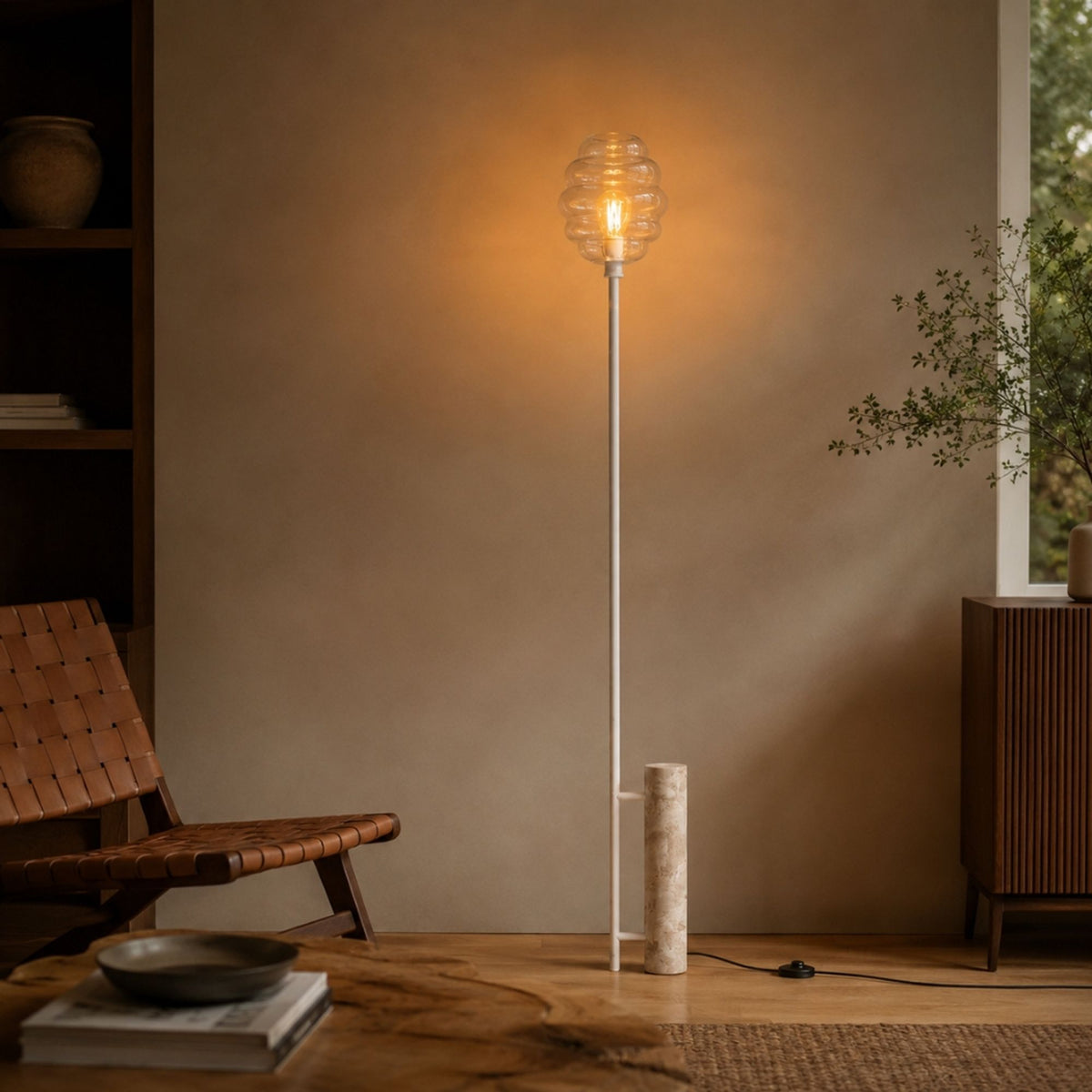 Intérieur avec fauteuil en cuir tressé et lampadaire allumé contre le mur beige.