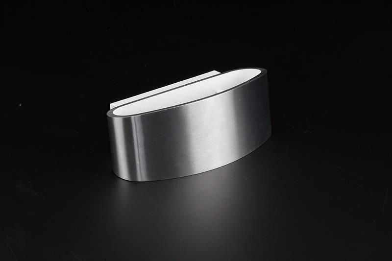 Vue de trois quarts sur fond noir, applique argentée courbée et diffuseur oval lumineux