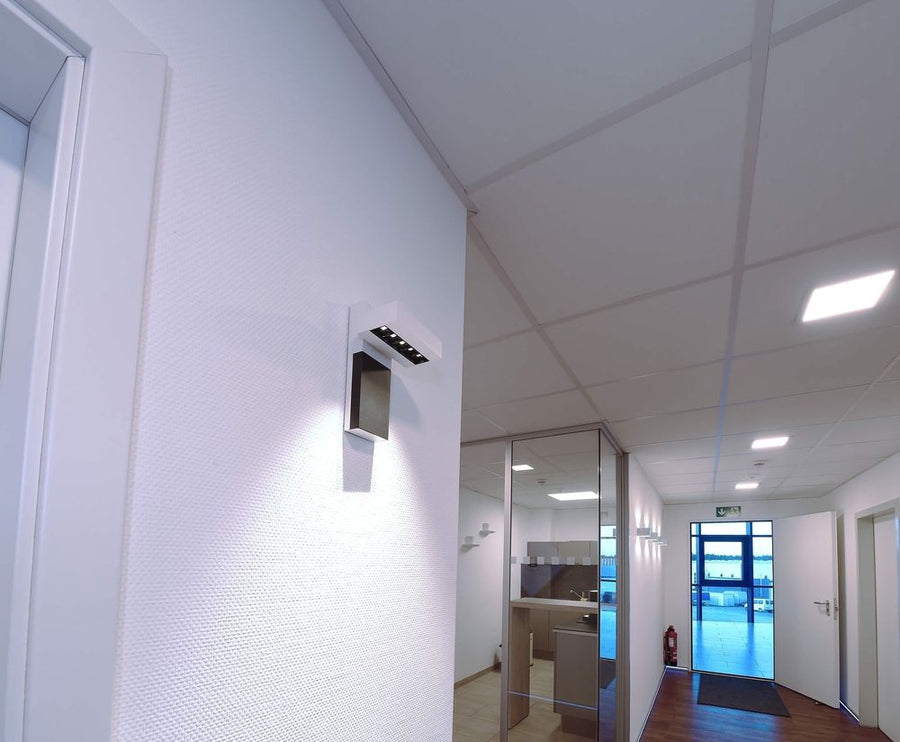Spot blanc installé sur un mur de couloir, éclairant le panneau mural.
