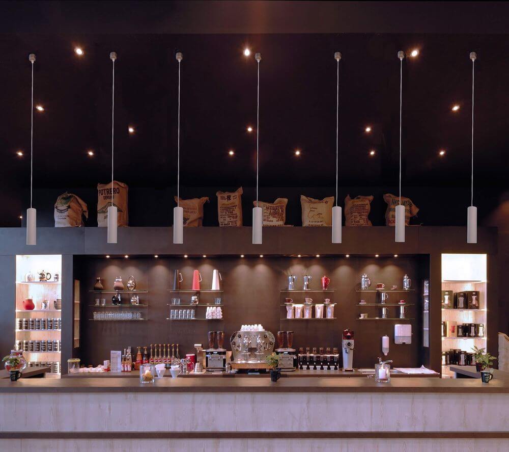 Plusieurs suspensions cylindriques en béton alignées au-dessus d’un comptoir de café.