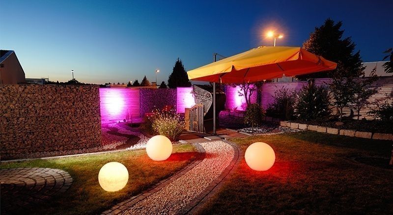 Jardin nocturne avec trois globes lumineux au sol près d'un chemin et d'un parasol