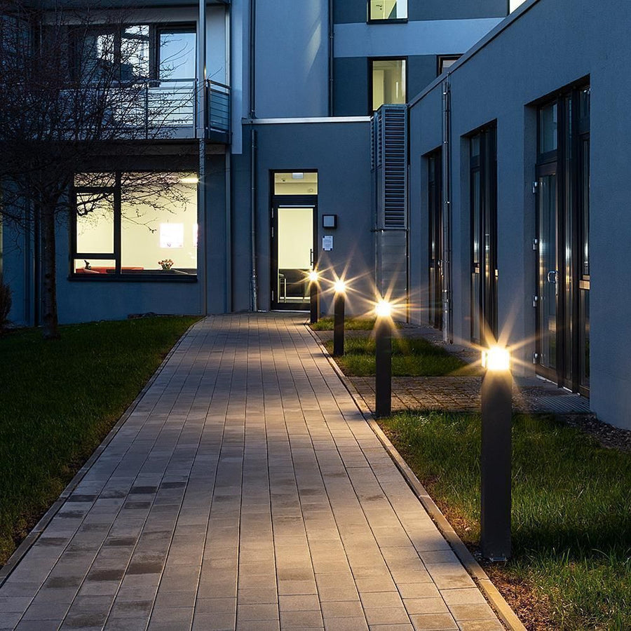 Plusieurs bornes éclairent une allée pavée le soir, halos lumineux en étoile.