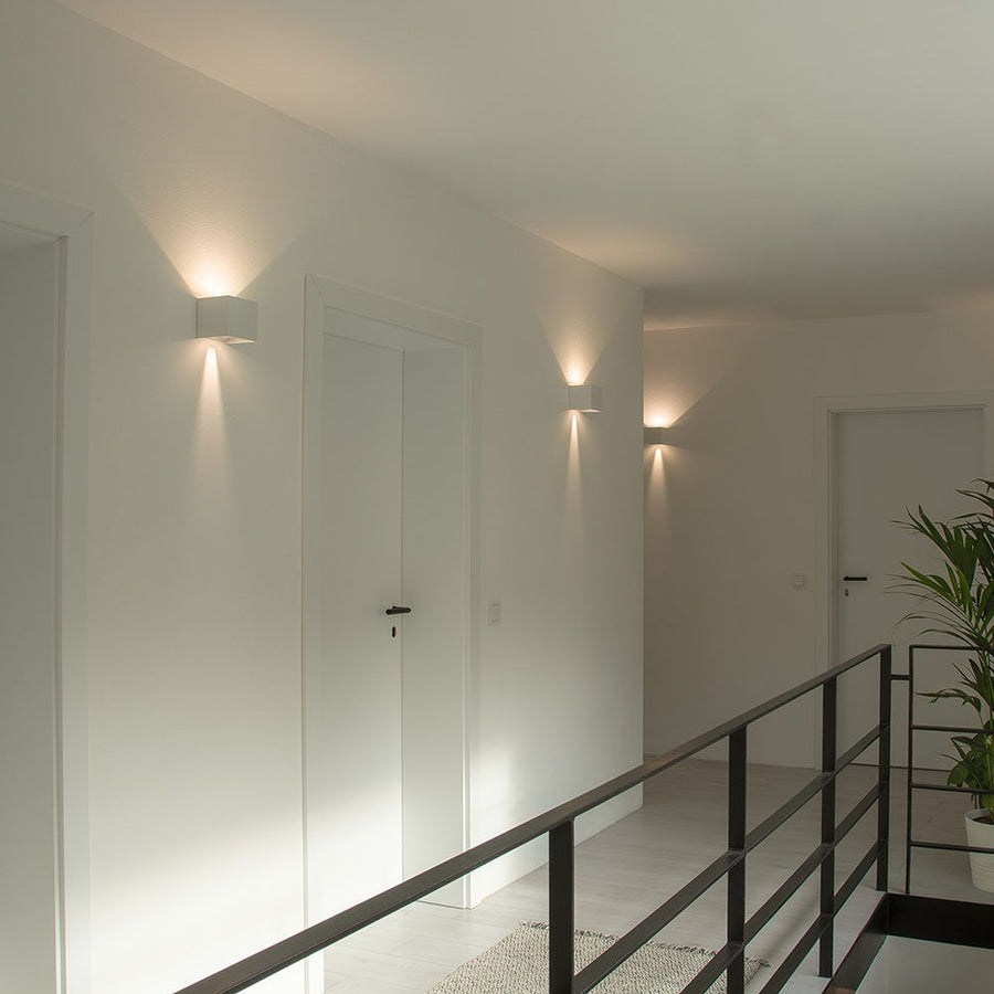 Couloir intérieur avec deux appliques blanches éclairant vers le haut et le bas.