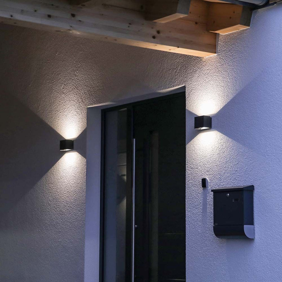 Entrée extérieure la nuit avec deux appliques noires encadrant une porte vitrée.