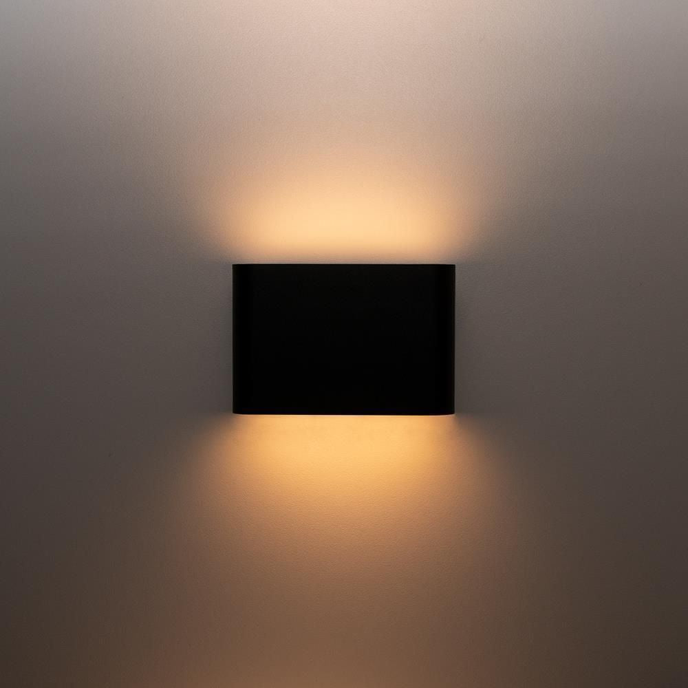 Applique noire allumée projetant deux faisceaux lumineux sur mur.