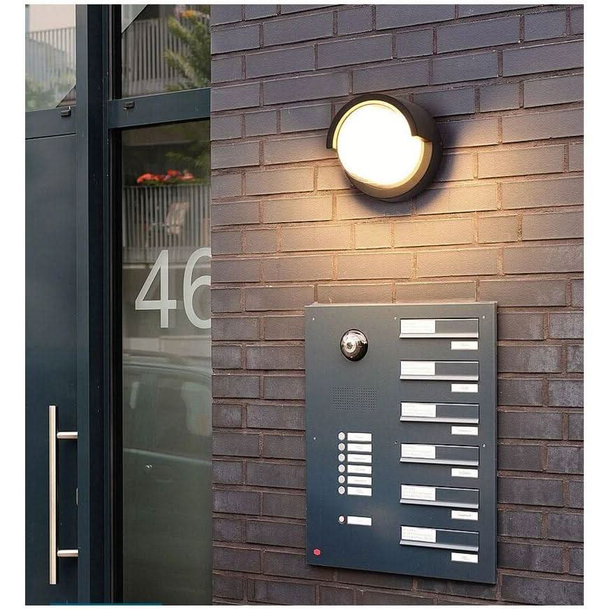 Luminaire mural extérieur fixé près d'une porte, interphone et boîtes aux lettres visibles.