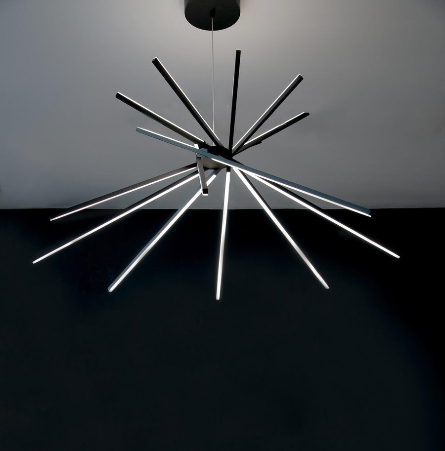 Vue de face du luminaire allumé, tiges noires rayonnantes sur fond sombre