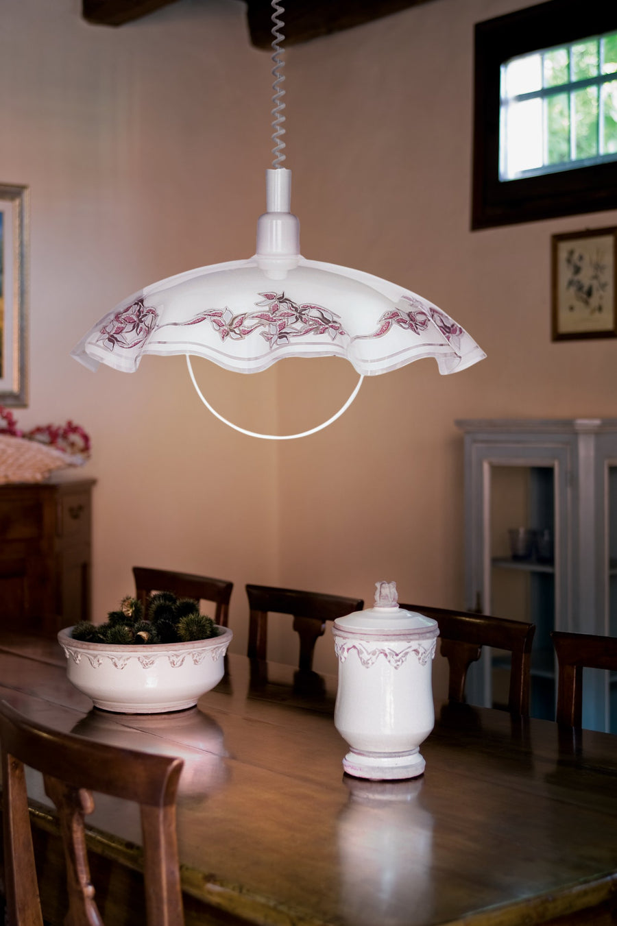 Suspension allumée au-dessus d'une table en bois, décor floral violet, intérieur rustique et chaleureux.