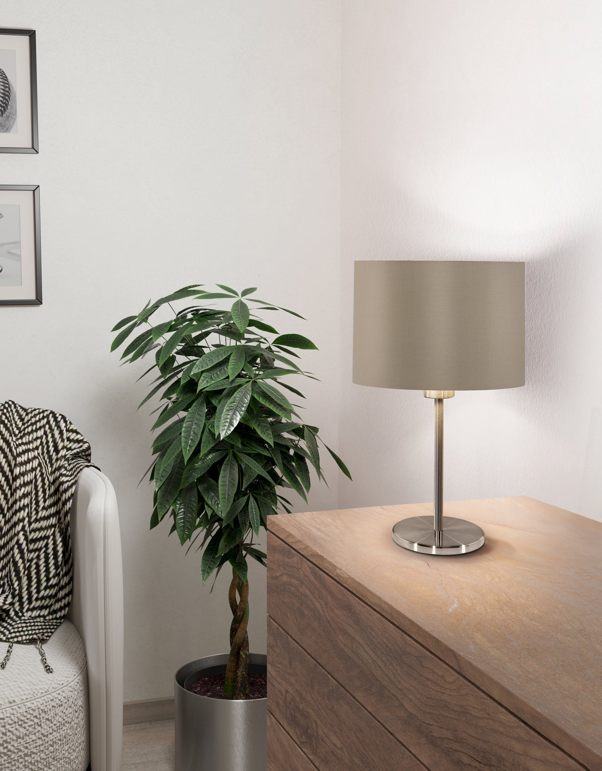 Lampe allumée posée sur un meuble en bois, à côté d'une plante verte