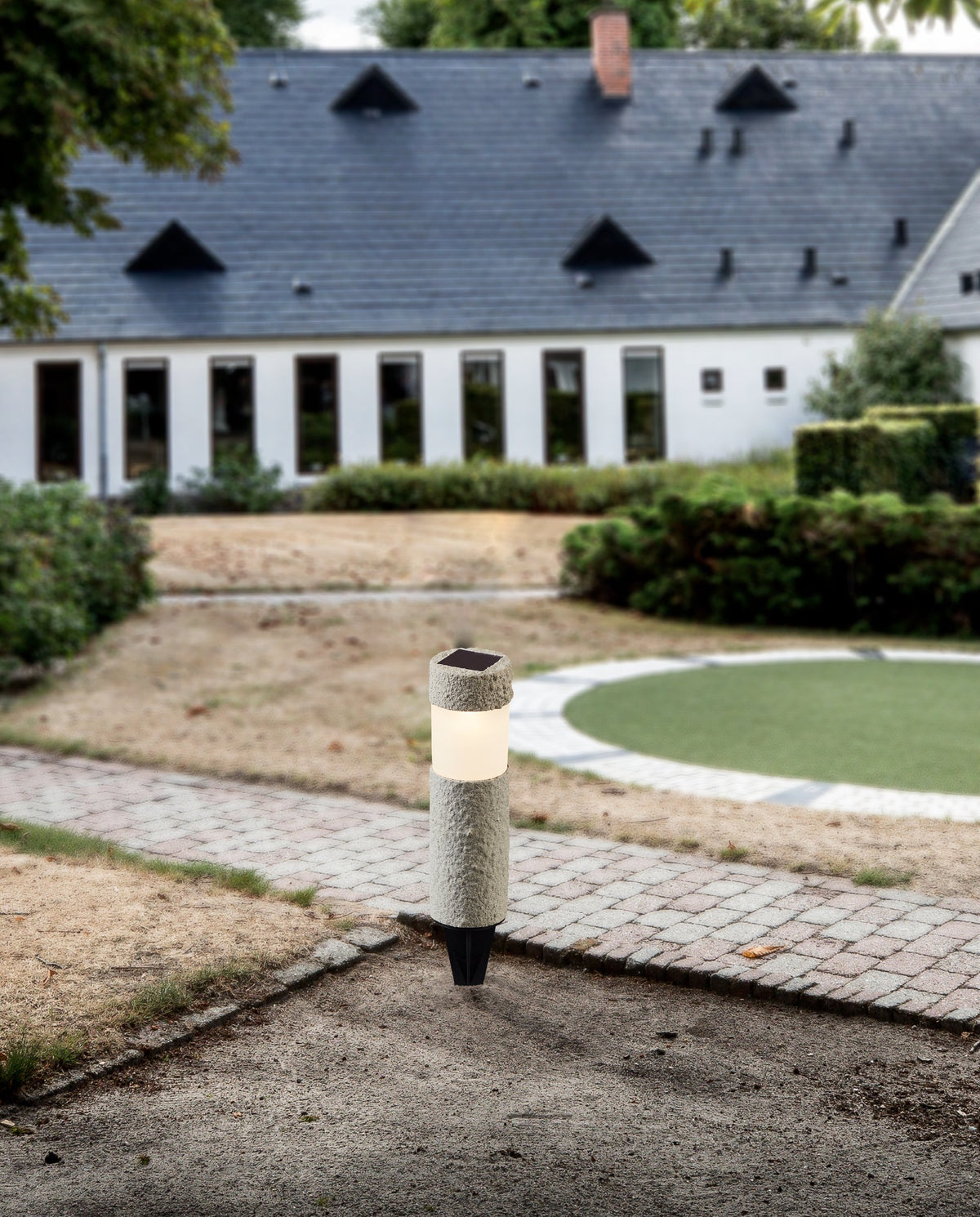 Luminaire solaire planté dans un jardin, devant une maison aux nombreuses fenêtres