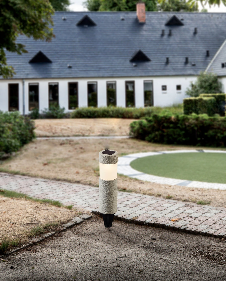 Luminaire solaire planté dans un jardin, devant une maison aux nombreuses fenêtres