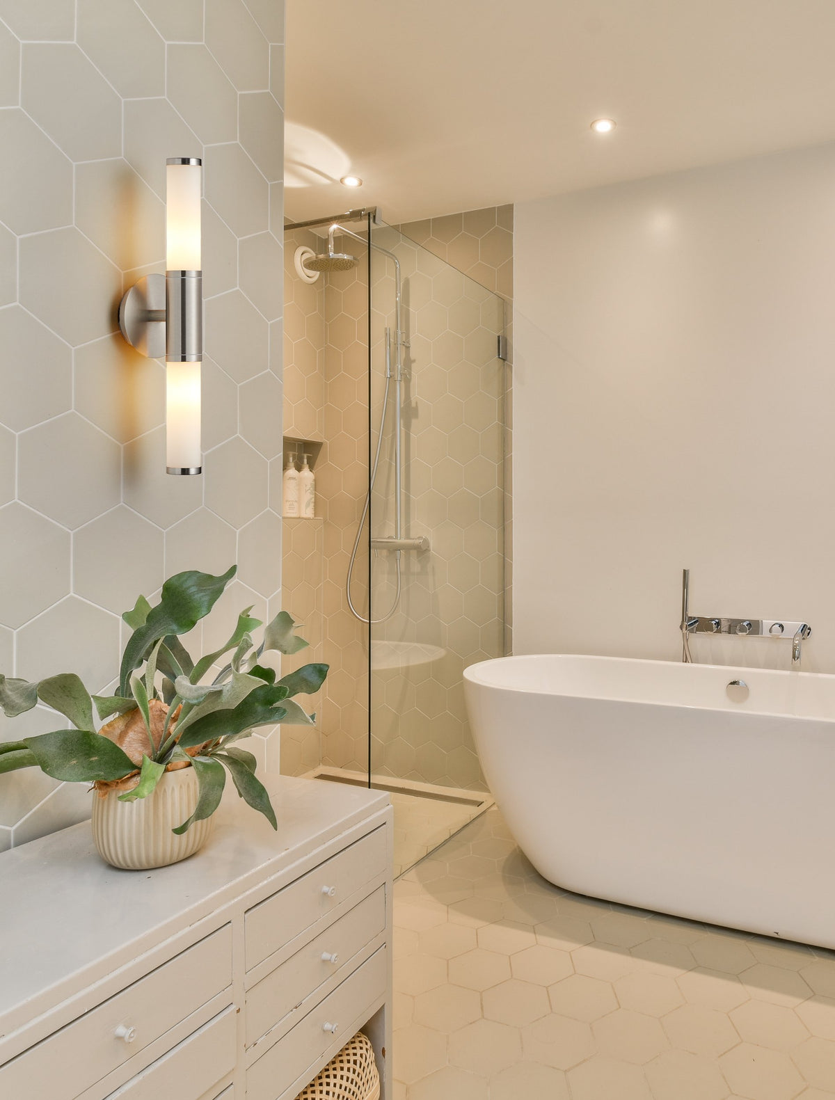 Mise en ambiance salle de bain avec applique allumée, baignoire îlot et paroi de douche