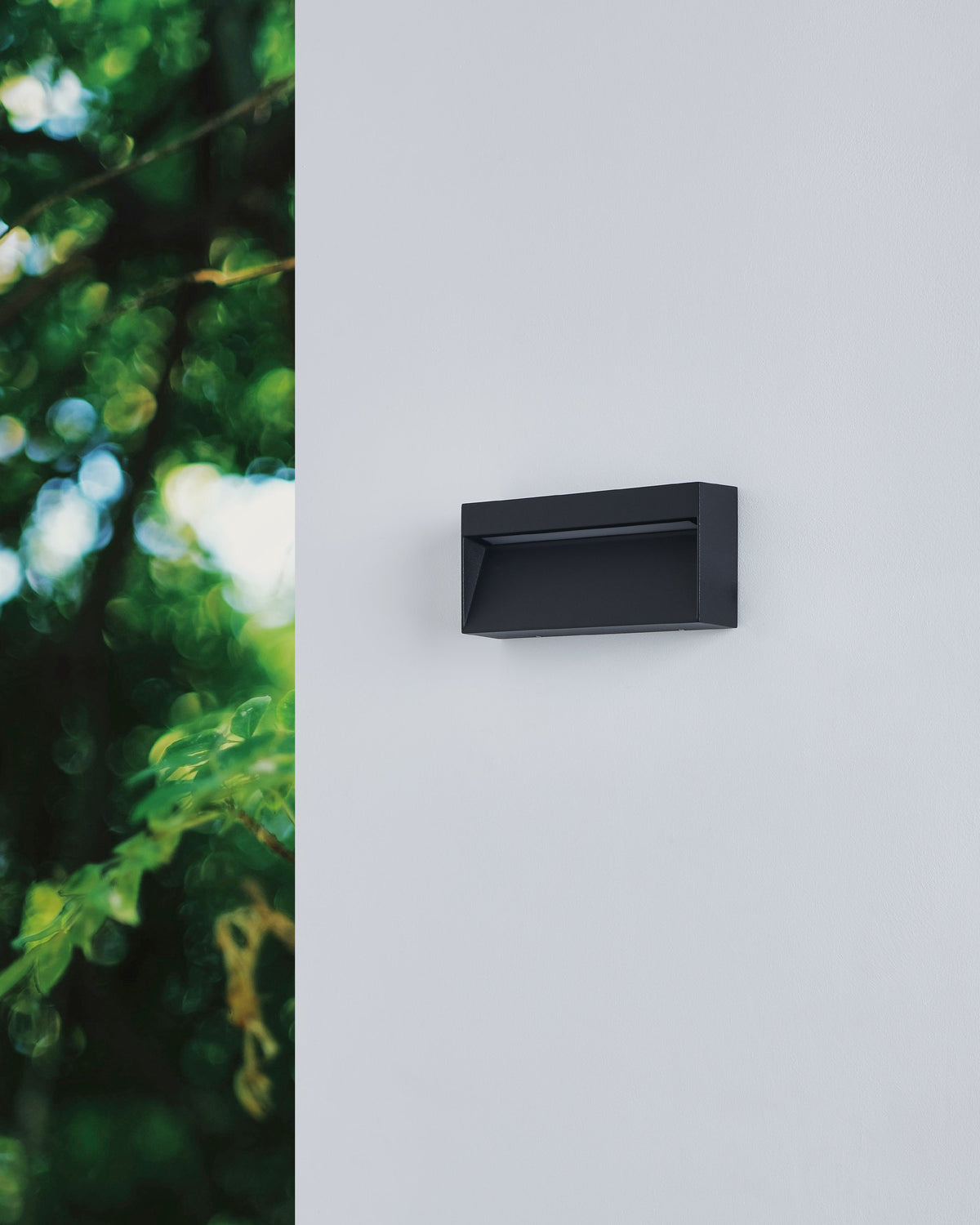 Applique murale noire éteinte fixée sur un mur blanc près de plantes