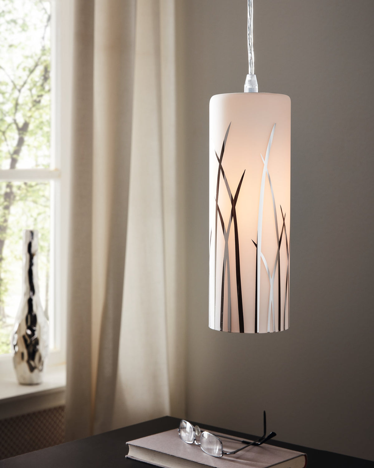 Suspension allumée dans un intérieur, avec rosace chromée et cylindre en verre.