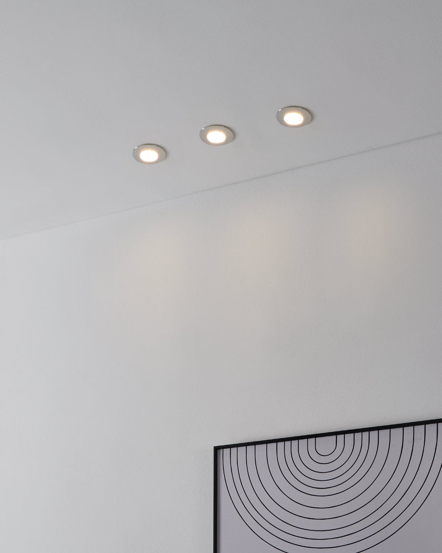 Trois spots encastrés allumés au plafond blanc, lumière chaude diffuse