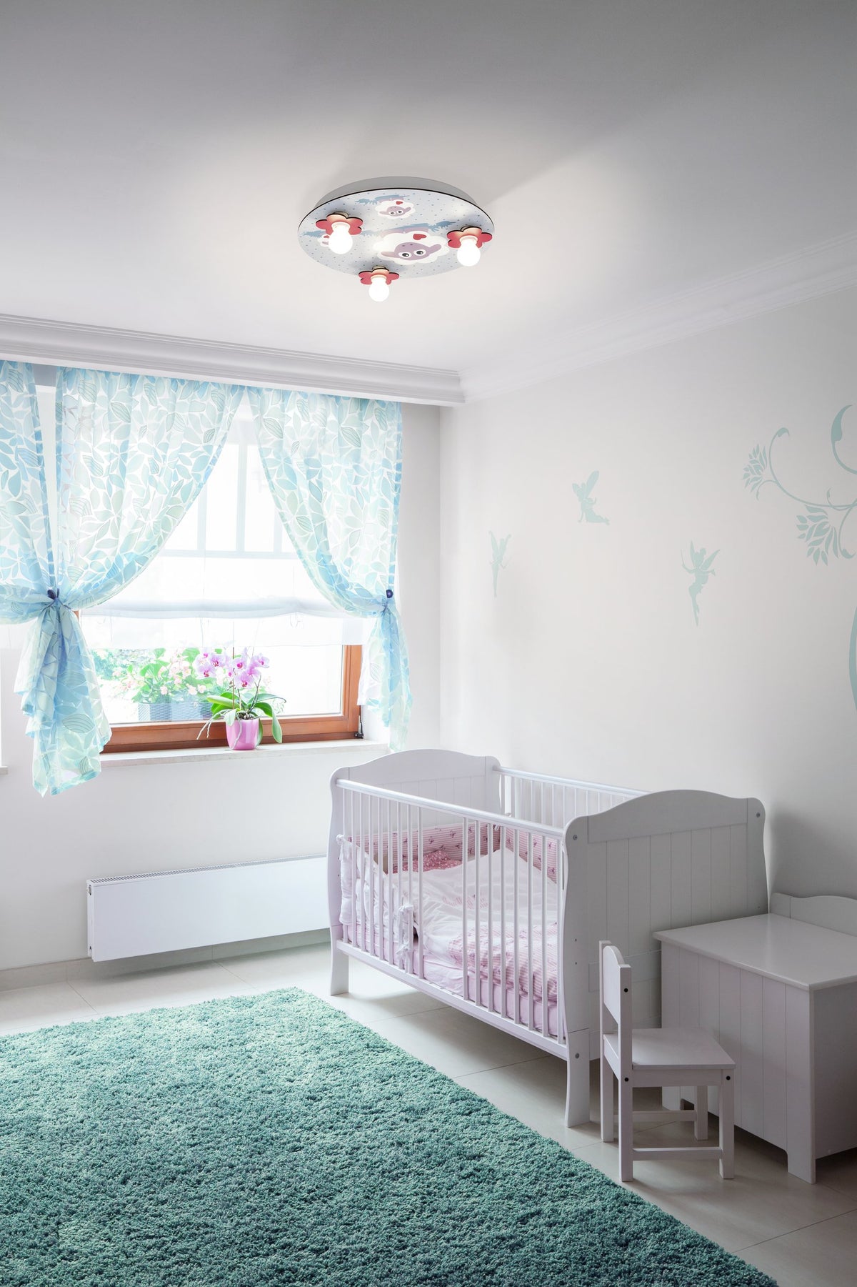 Mise en ambiance du plafonnier dans une chambre d'enfant avec lit à barreaux, tapis vert et rideaux bleus.