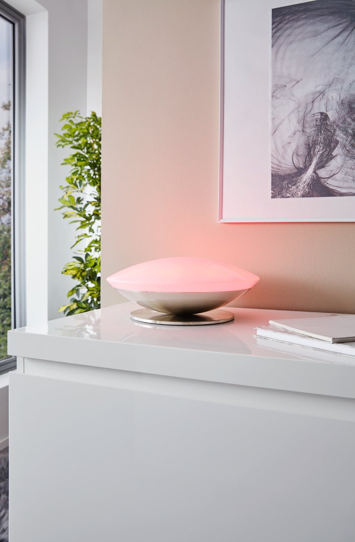 Gros plan du luminaire posé sur un buffet blanc, lumière rose et cadre au mur
