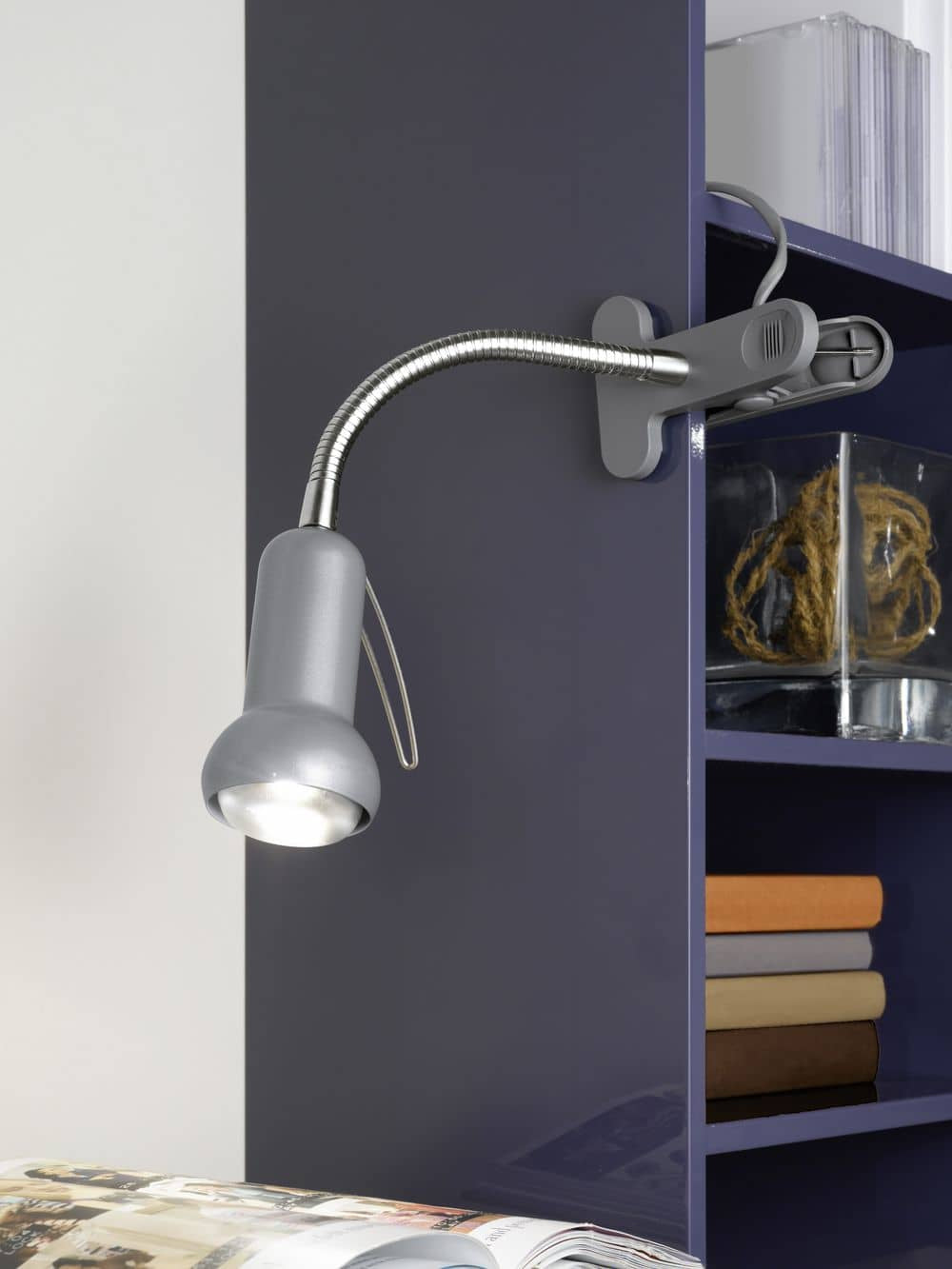 Lampe à pince accrochée à une étagère, éclairant un magazine ouvert et des livres.