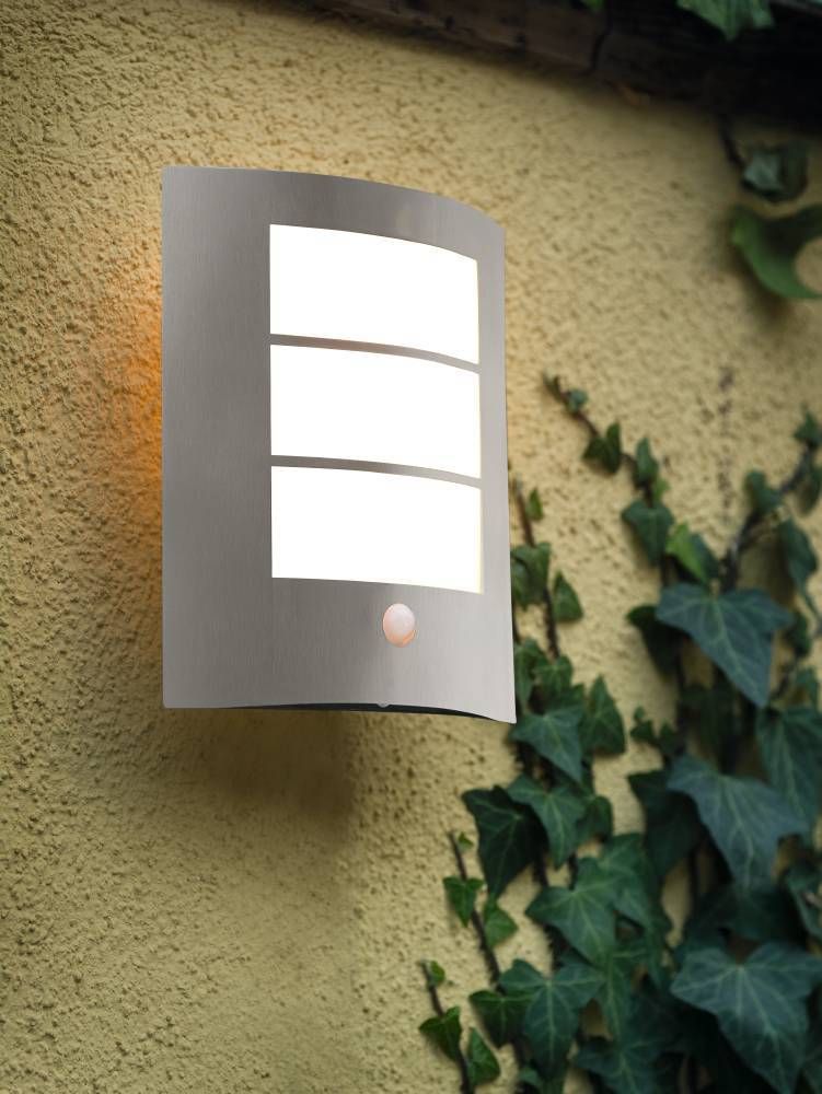 Luminaire extérieur éclairé fixé sur mur crépis jaune, entouré de lierre grimpant