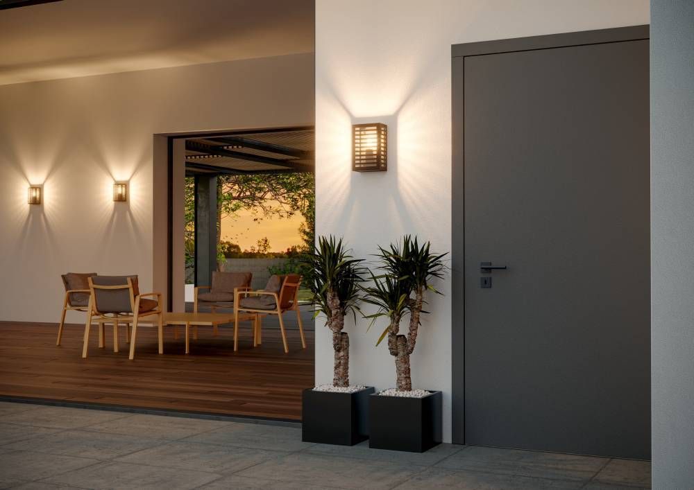 Mise en ambiance crépusculaire : applique murale allumée près d'une porte, terrasse avec fauteuils.