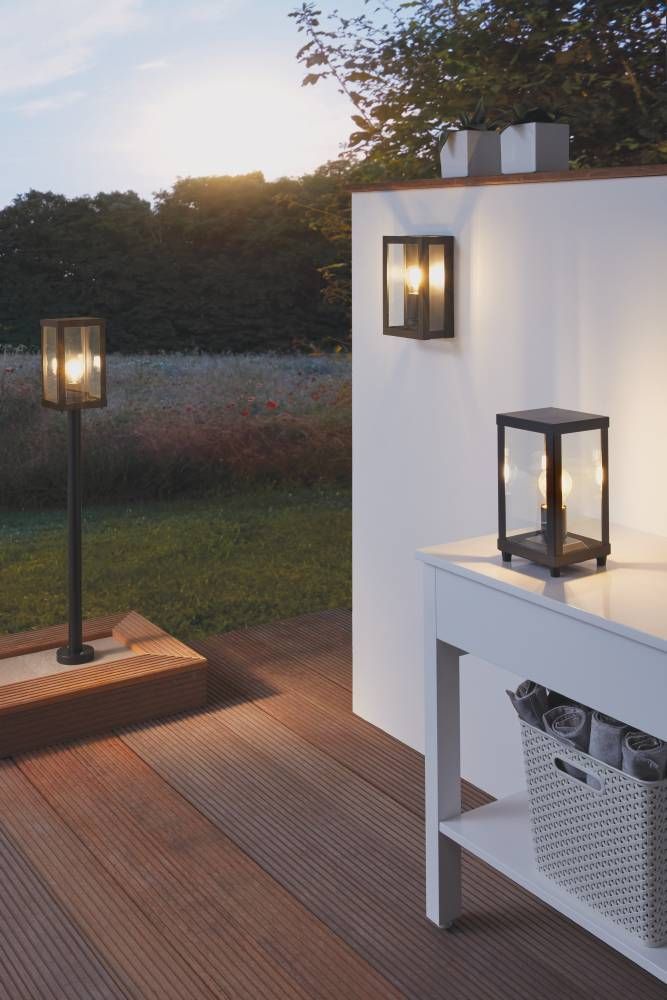 Mise en ambiance crépusculaire sur une terrasse en bois, applique, lampadaire et lampe de table assortis