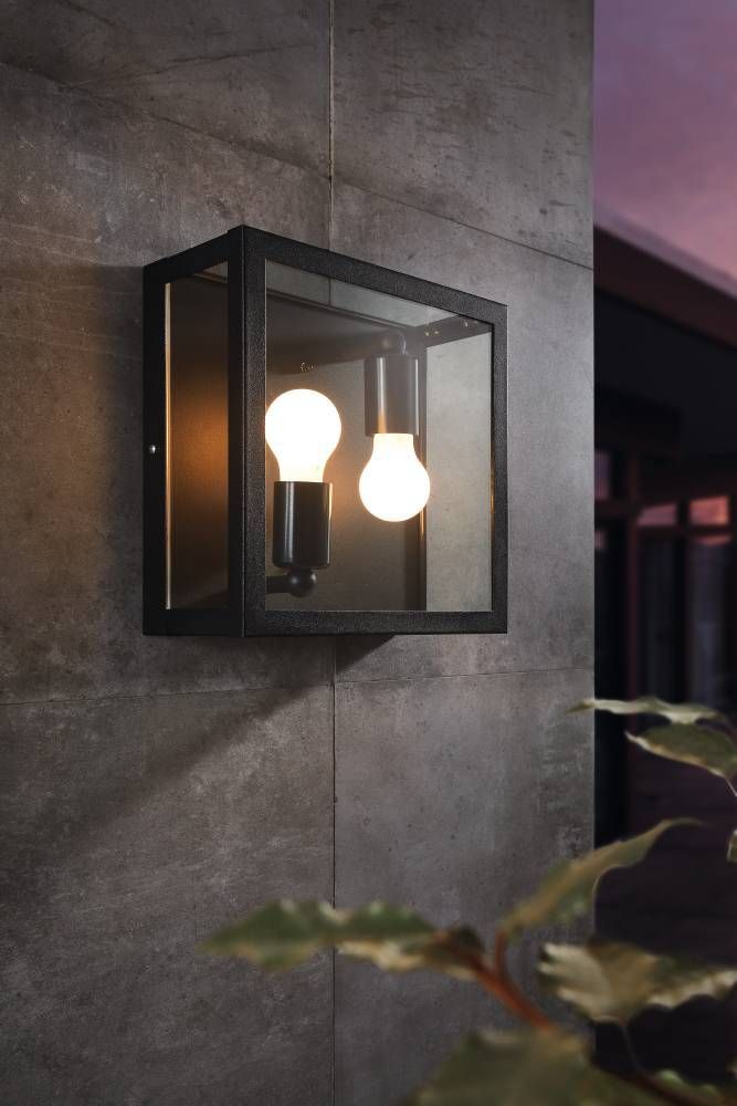Applique murale noire en métal et verre installée sur un mur béton, deux ampoules allumées.
