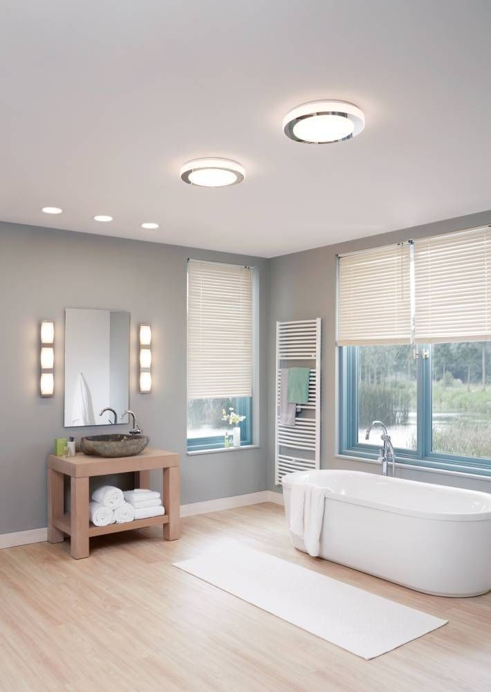 Salle de bain moderne avec deux plafonniers ronds allumés au plafond et baignoire.