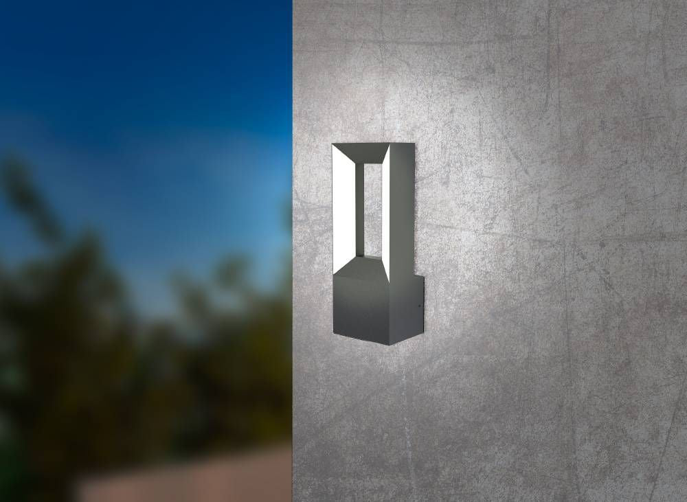 Applique extérieure noire et blanche éclairée, fixée sur un mur gris, ciel et feuillage flous