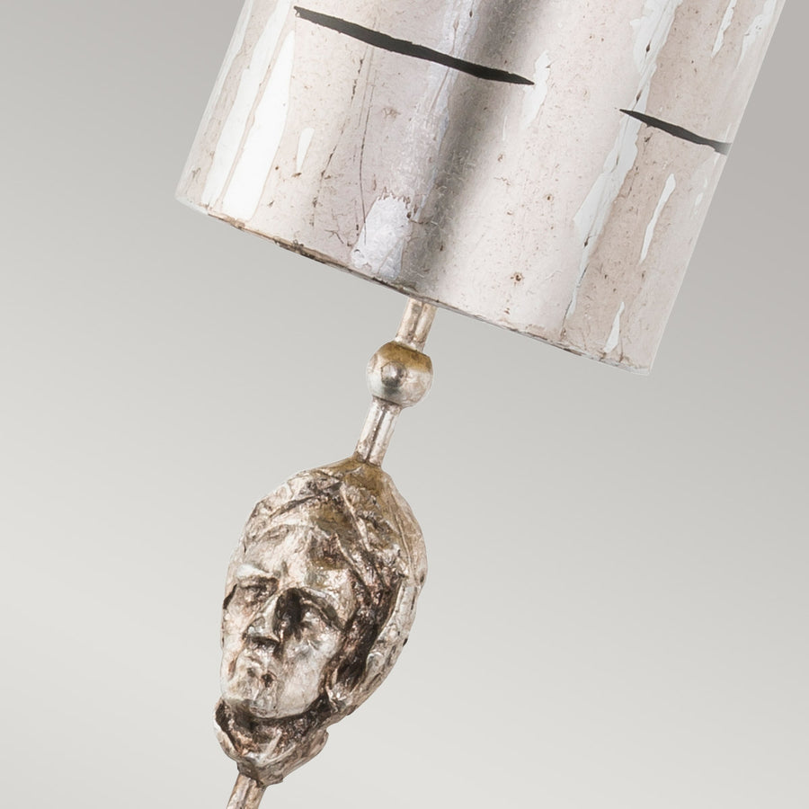 Gros plan sur la tête sculptée argentée sous l'abat-jour et sa tige.