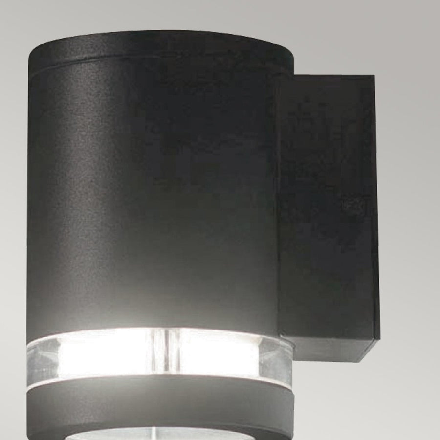Gros plan de l'applique cylindrique noire, diffuseur annulaire lumineux sous le corps.
