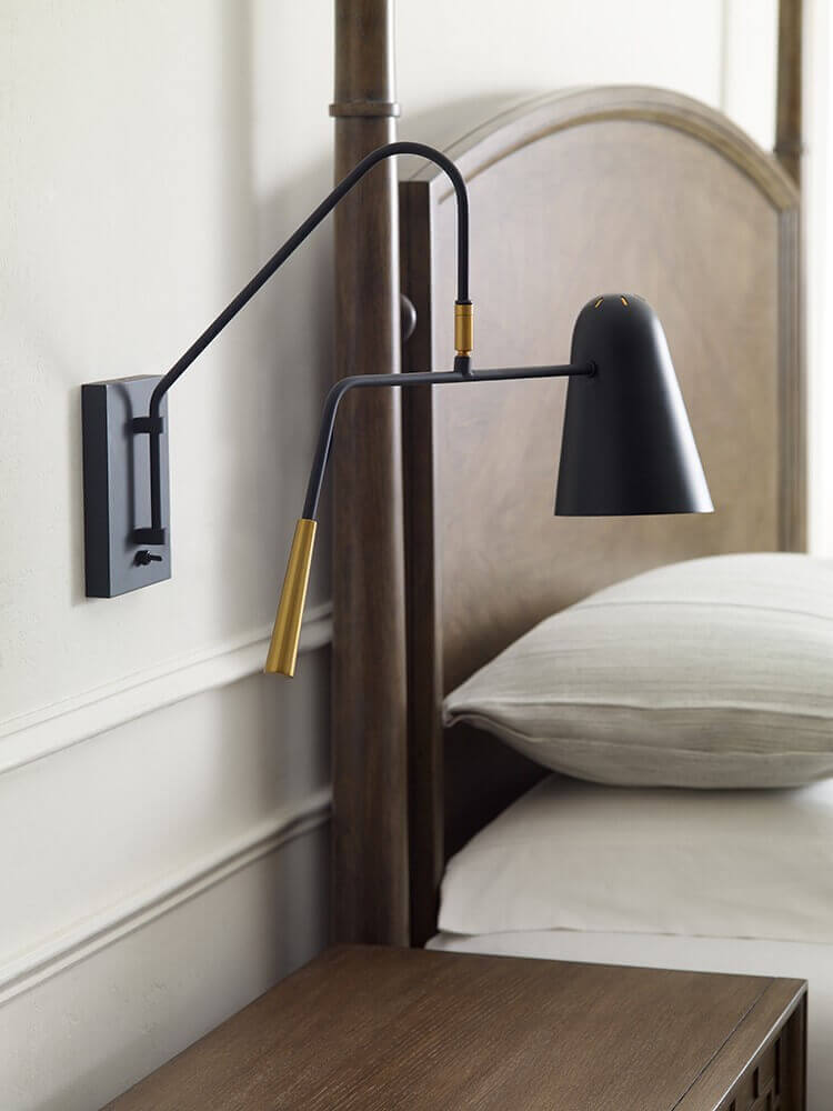 Applique noire installée en tête de lit en bois, au-dessus d'un oreiller blanc