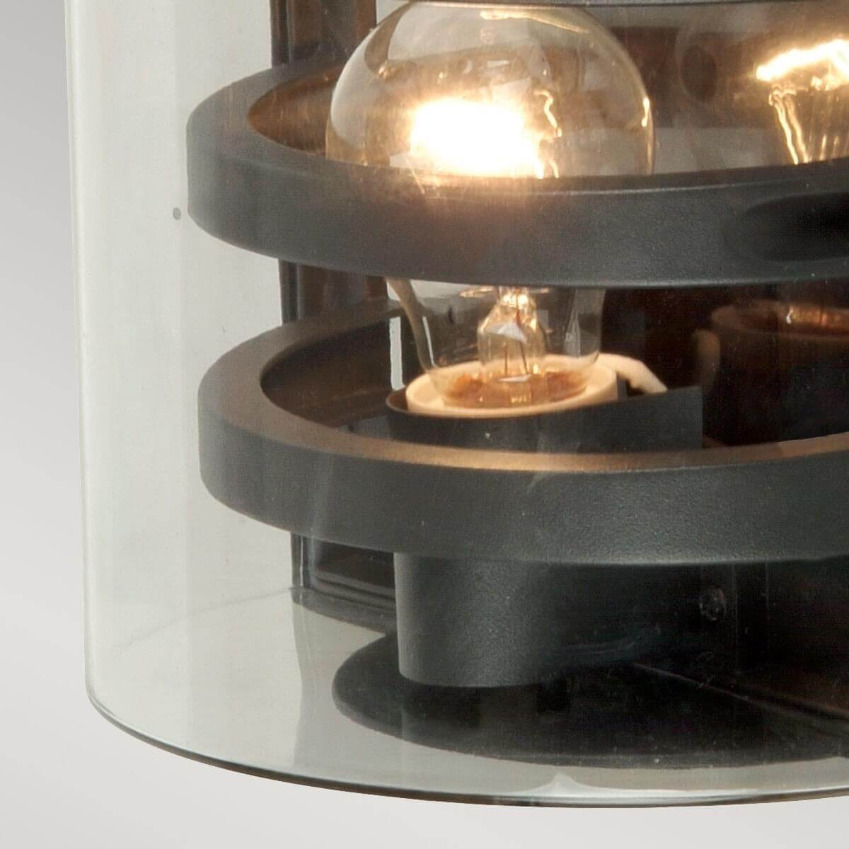 Gros plan sur l’ampoule éclairée et les anneaux métalliques du luminaire extérieur.