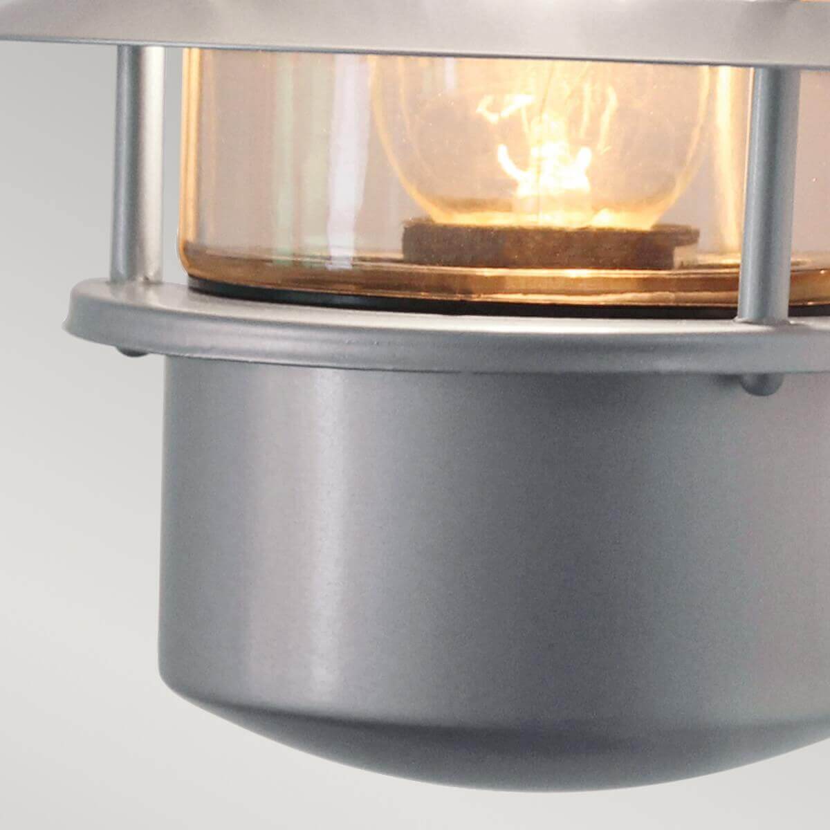 Détail du bas du luminaire, verre ambré et ampoule allumée à l'intérieur.