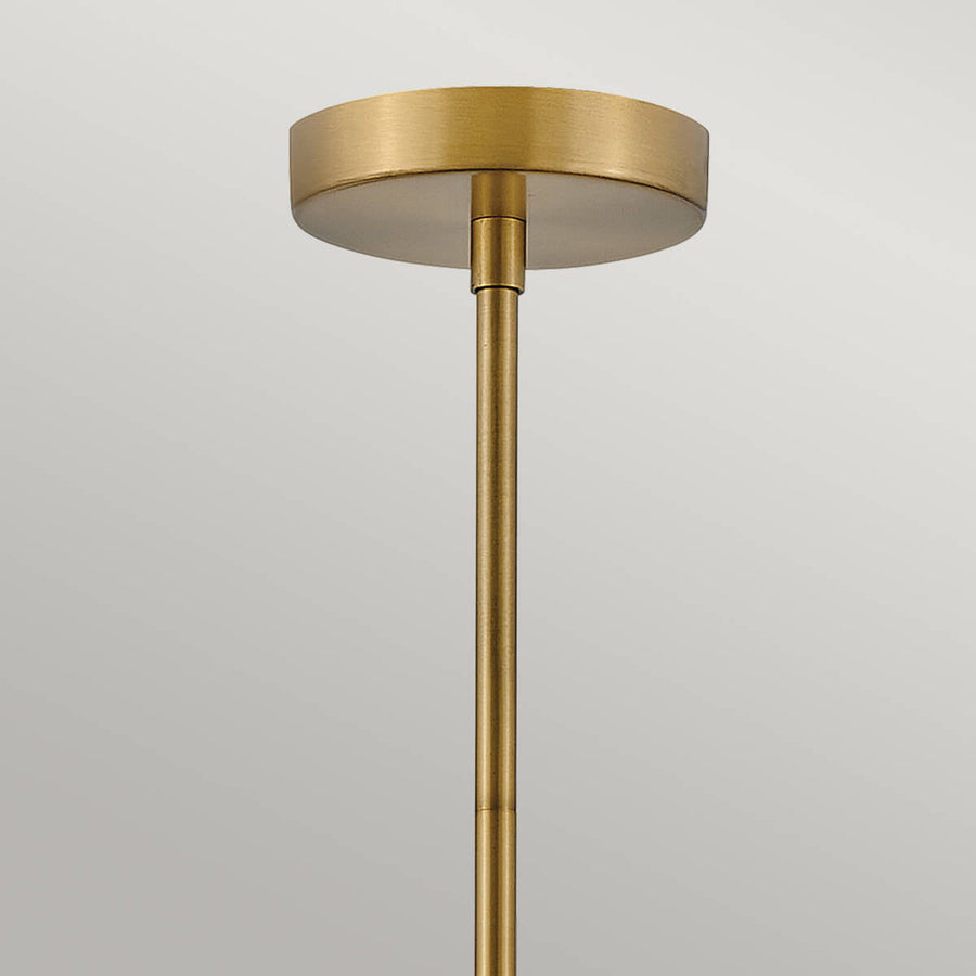 Rosace ronde en laiton fixée au plafond et tige dorée verticale.